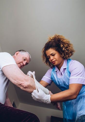 Nurse applying bandage to patient's arm; both are indoors.