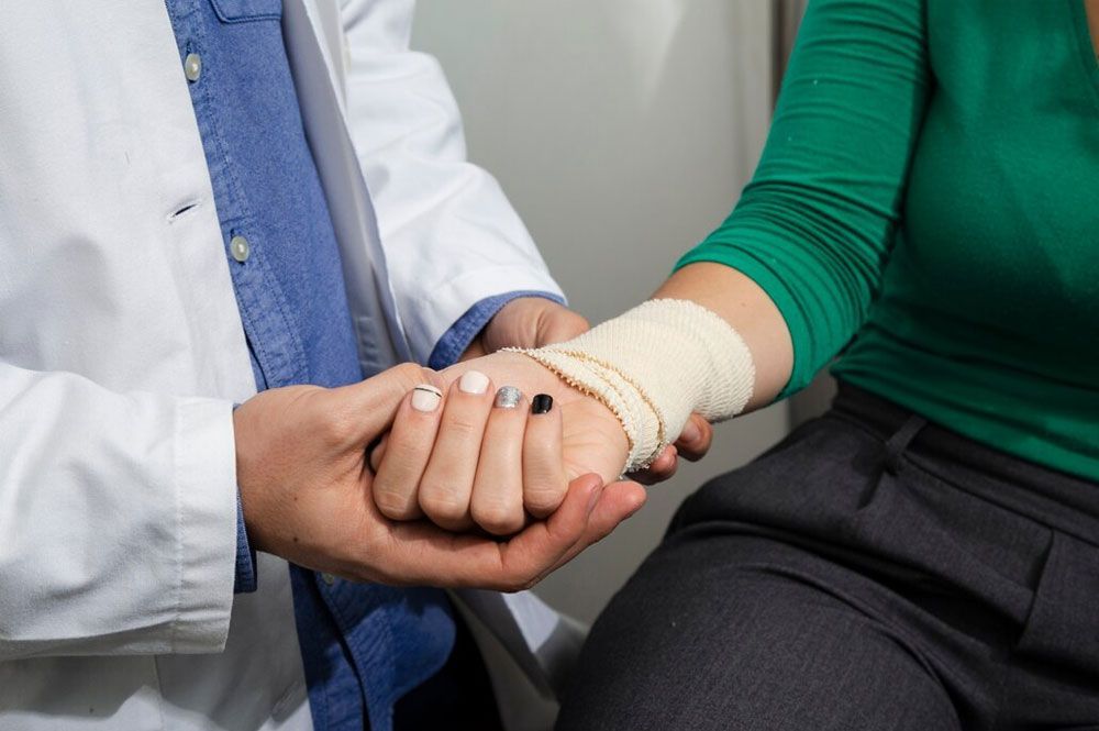 Doctor holding the bandaged wrist of a patient in a medical setting.