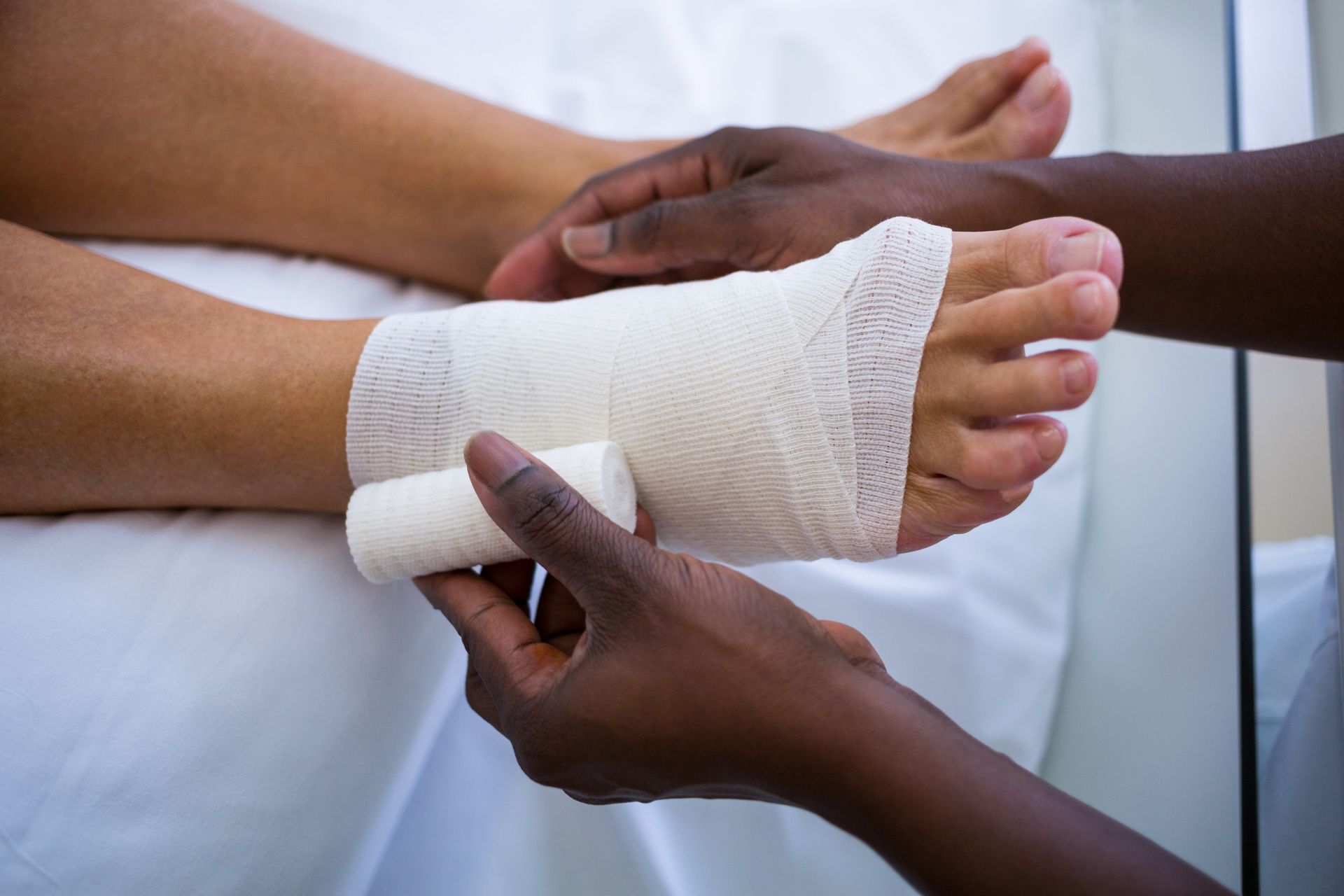 Person's foot being bandaged by another person on a white surface.
