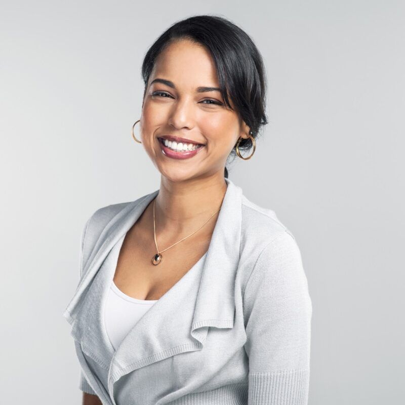 Woman with dark hair smiles, wearing a light gray cardigan over a white top, against a gray background.