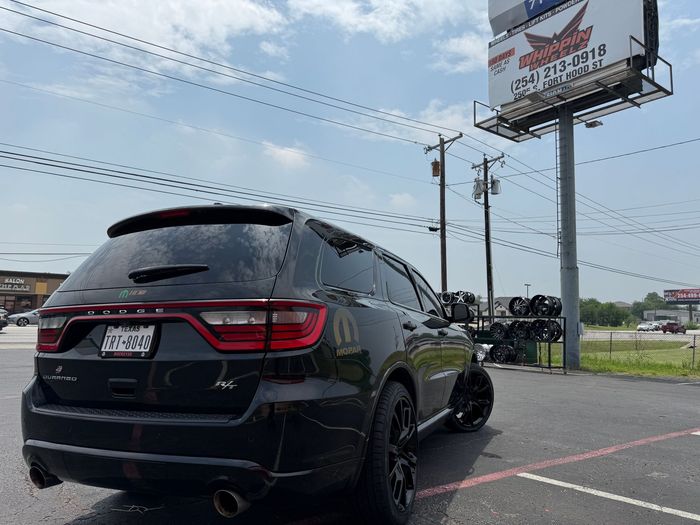 A black car is parked in a parking lot in front of a billboard.