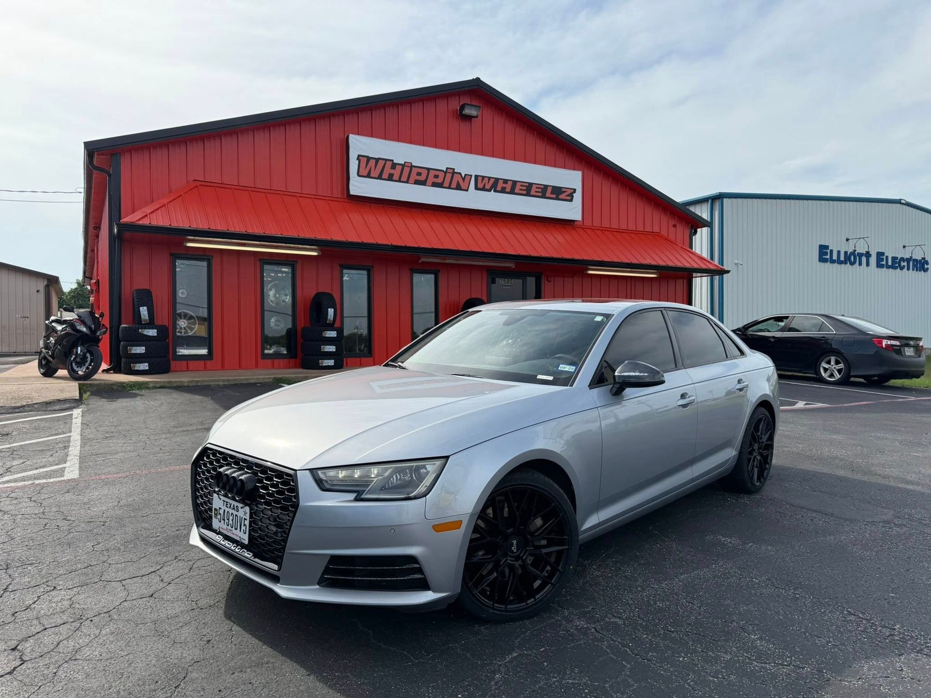 A silver audi a4 is parked in front of a red building.