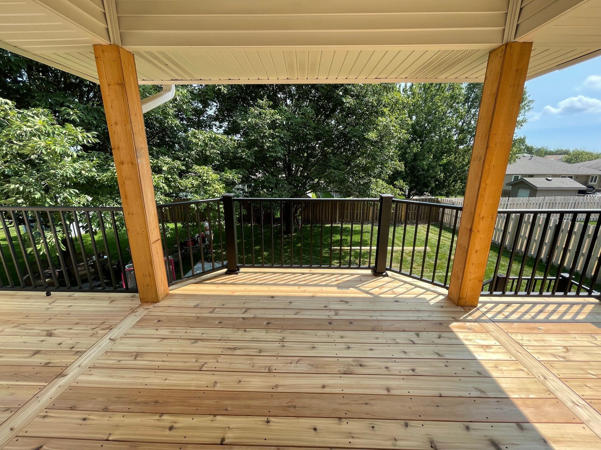 A wooden deck with a metal railing and a view of a backyard.