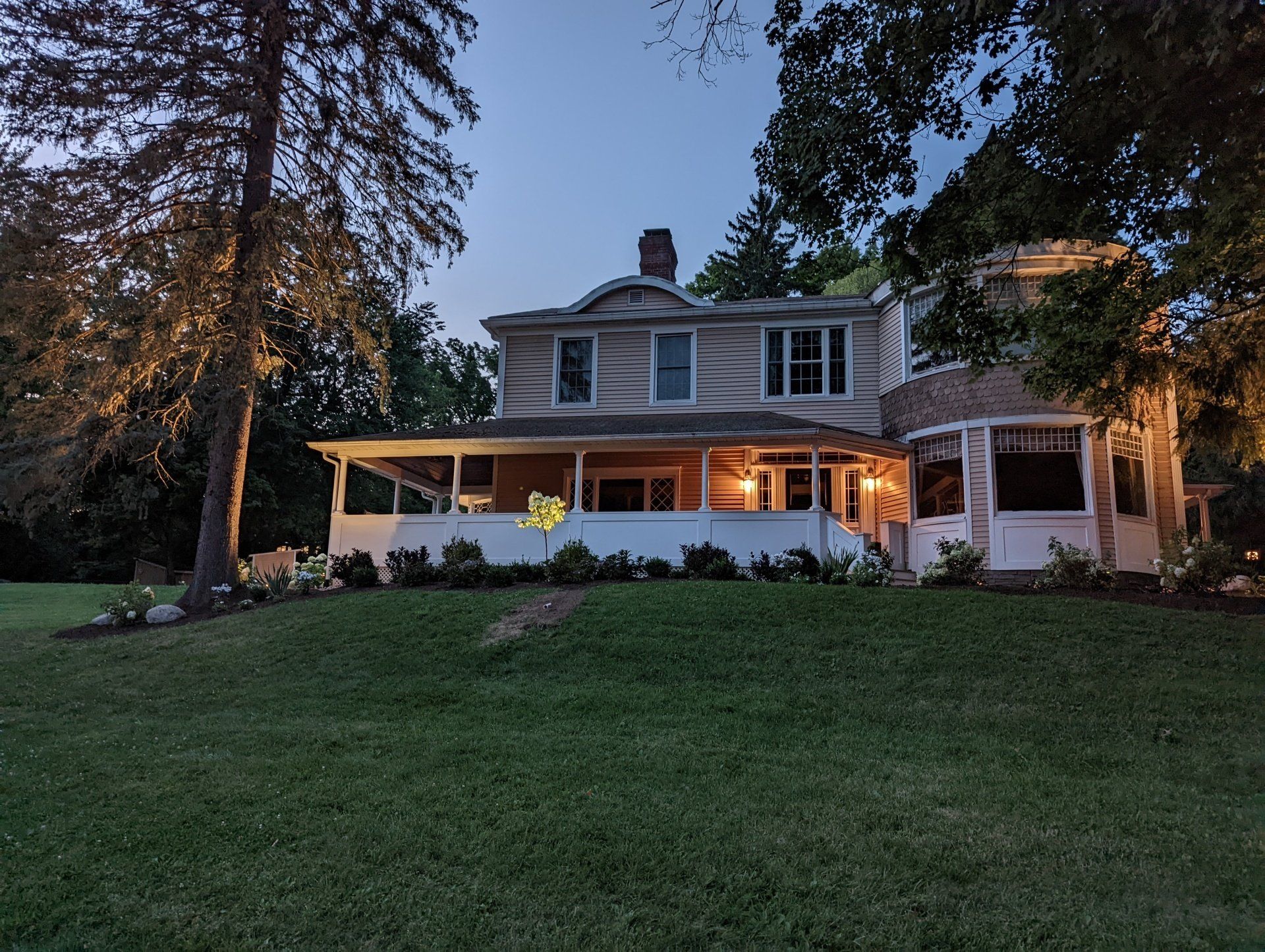 a large house with a large porch is lit up at night by landscape lights