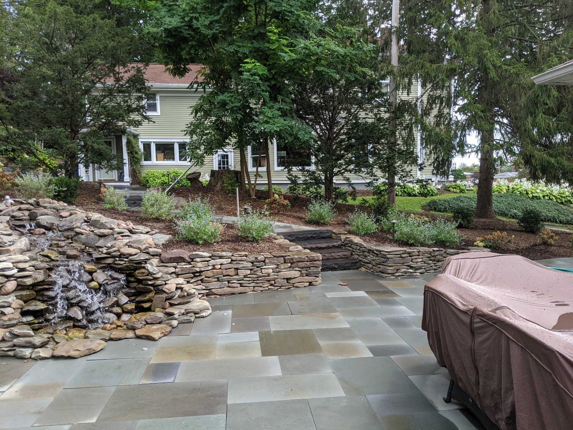 a  natural stone patio area with a waterfall and a house in the background