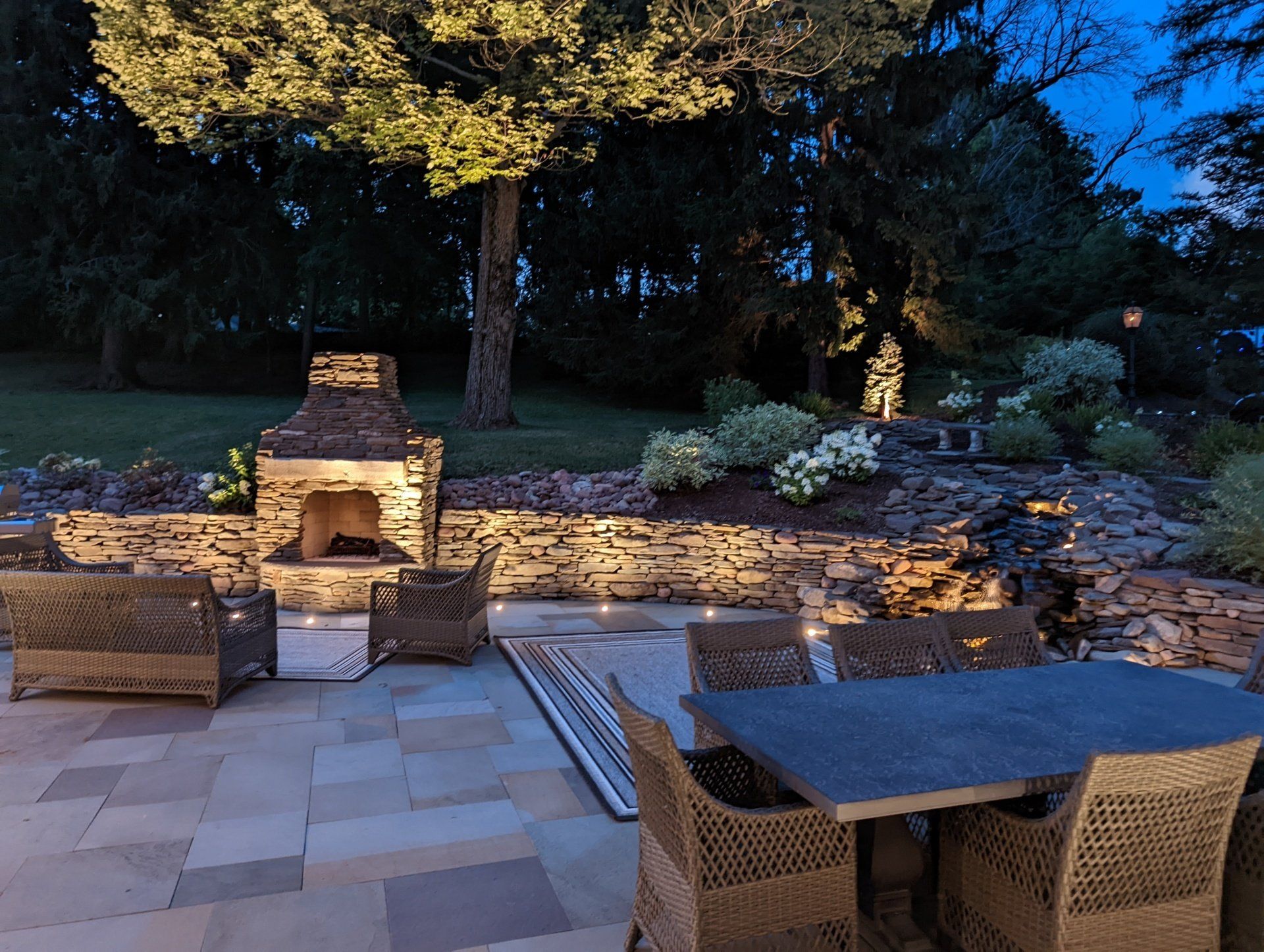 a patio with a table and chairs and a natural stone fireplace at night
