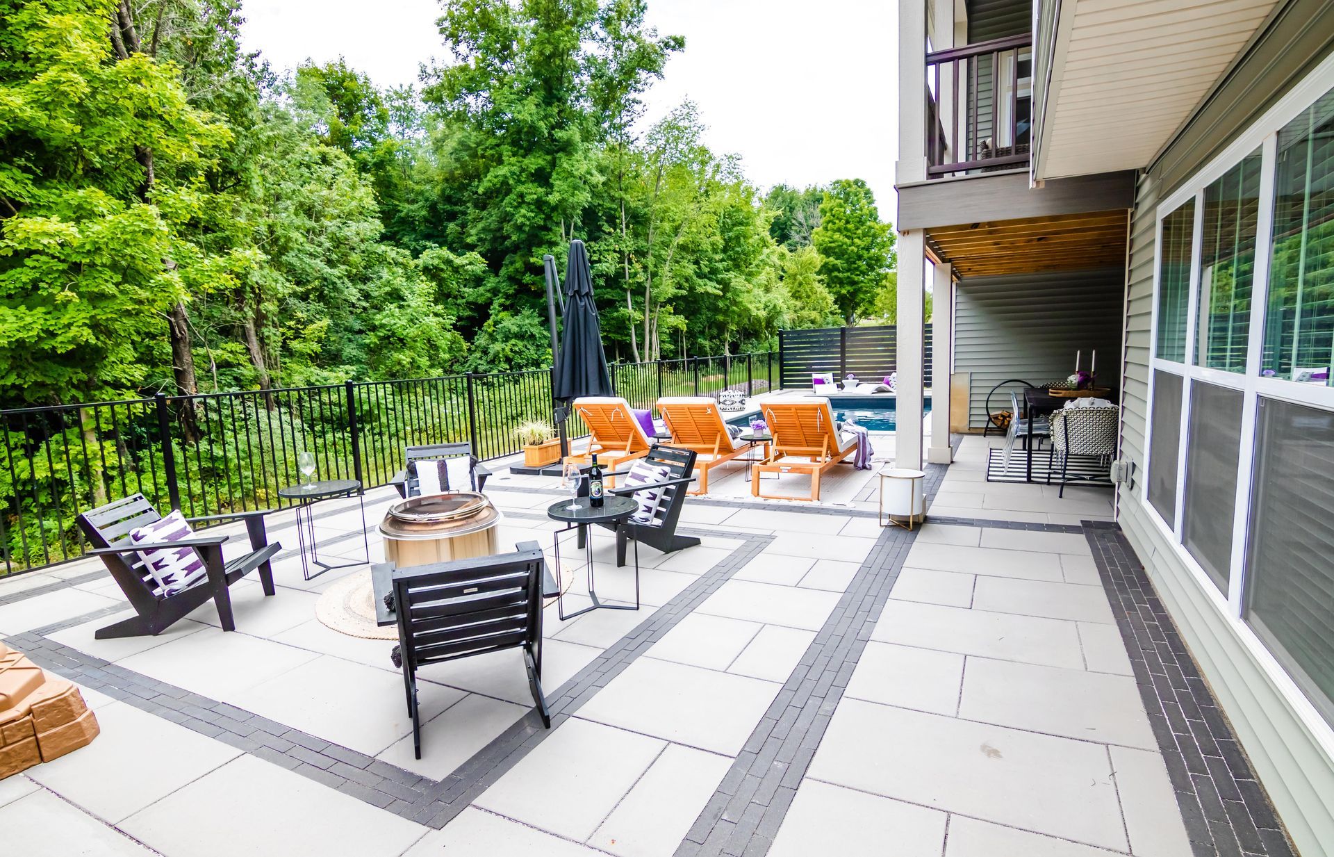 a large patio with a fire pit and chairs in front of a house and surrounding an in inground ppol 