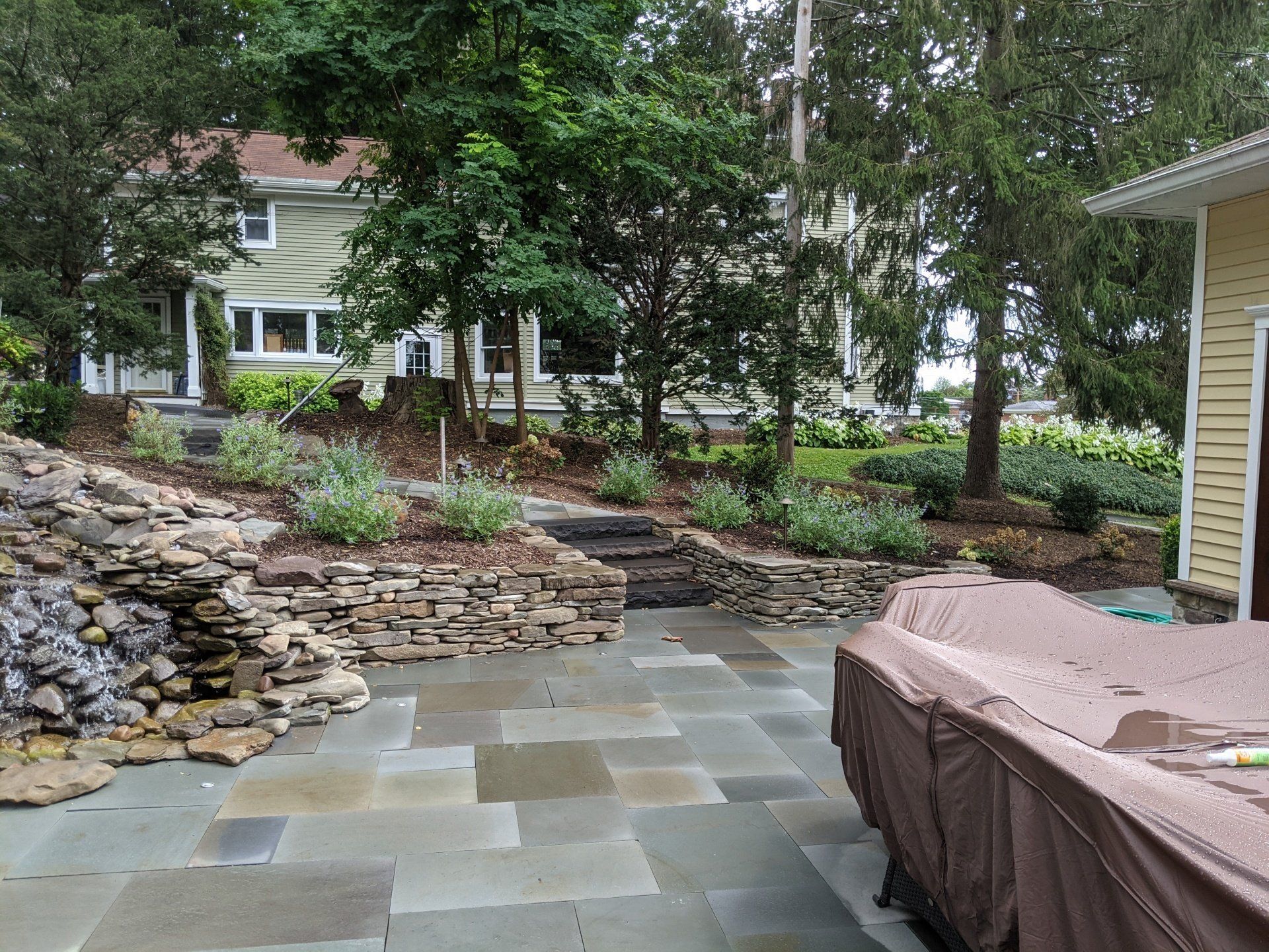a patio with a natural stone retaining wall and waterfall and a house in the background