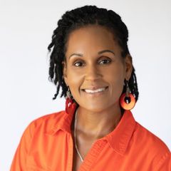 Smiling person in an orange shirt with black hair and orange earrings against a white background