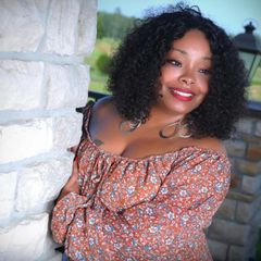 Smiling woman in an off-shoulder floral dress leaning against a stone wall outdoors