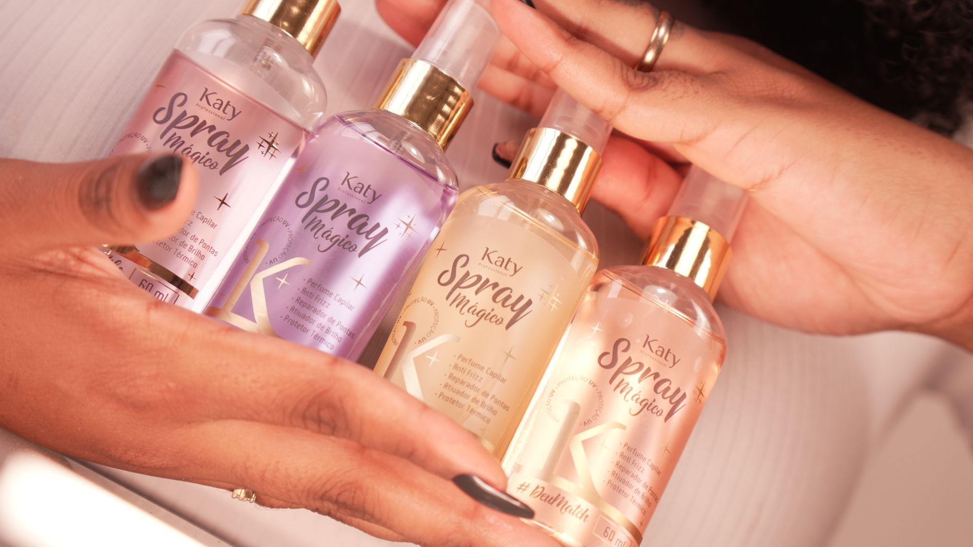 Mãos segurando quatro versões do Spray Mágico Katy