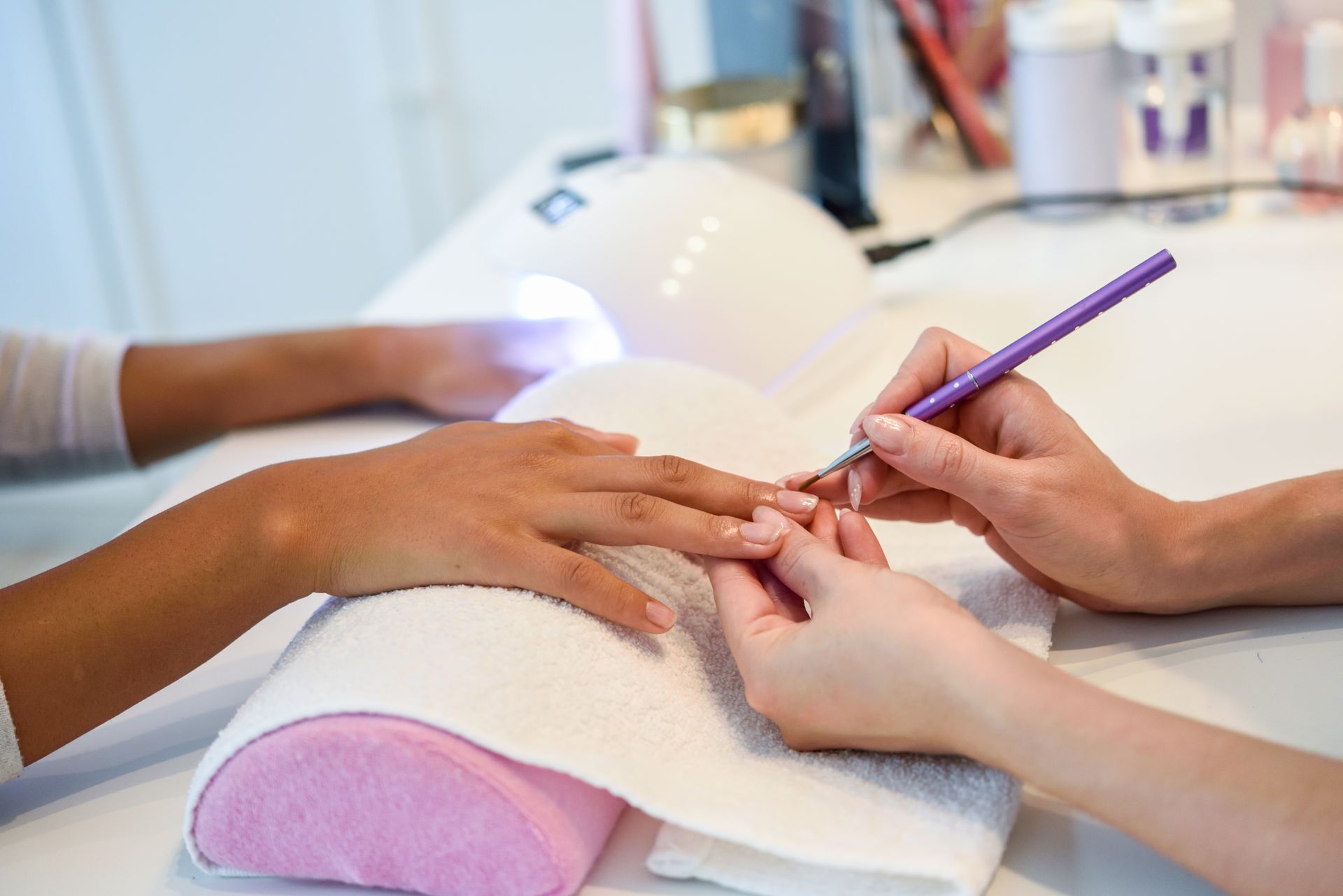 Esteticista aplicando produto com pincel em unhas alongadas de cliente em salão de beleza, com cabin