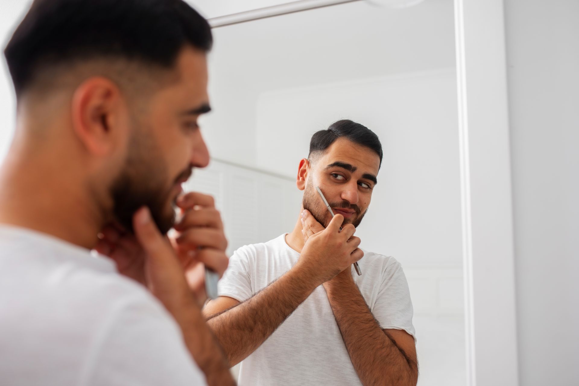 Homem alinhando a barba com navalha durante rotina de cuidados em casa.