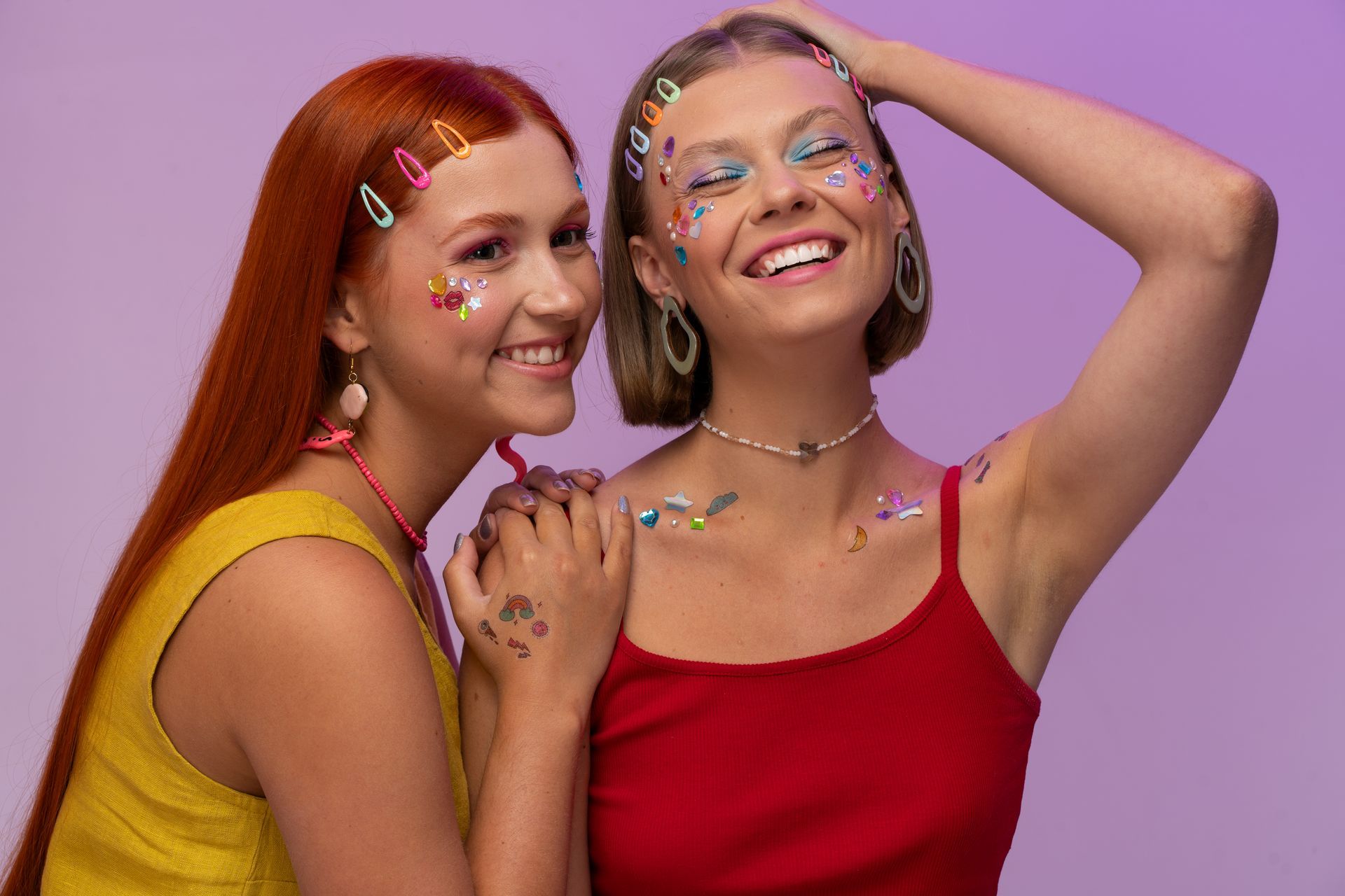 Amigas sorrindo com acessórios coloridos no cabelo e adesivos brilhantes de carnaval em fundo roxo.