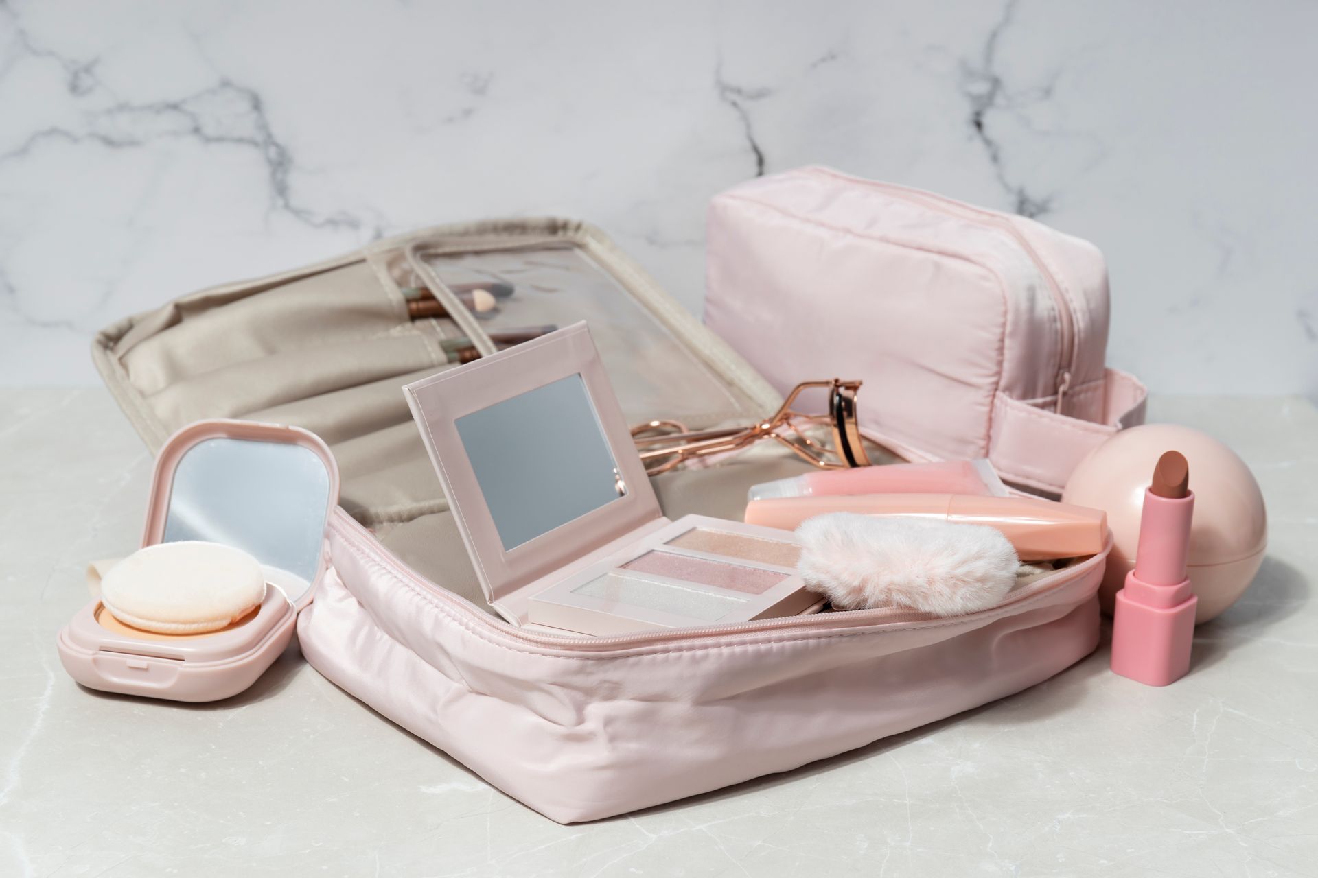 Necessaire rosa aberta com espelho e acessórios de beleza femininos organizados sobre bancada.