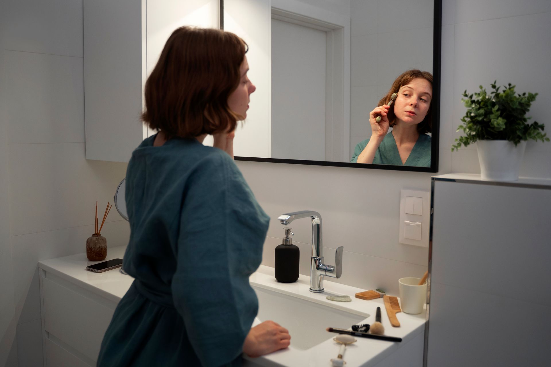 Mulher no banheiro na frente do espelho com produtos de beleza realizando skincare noturno.