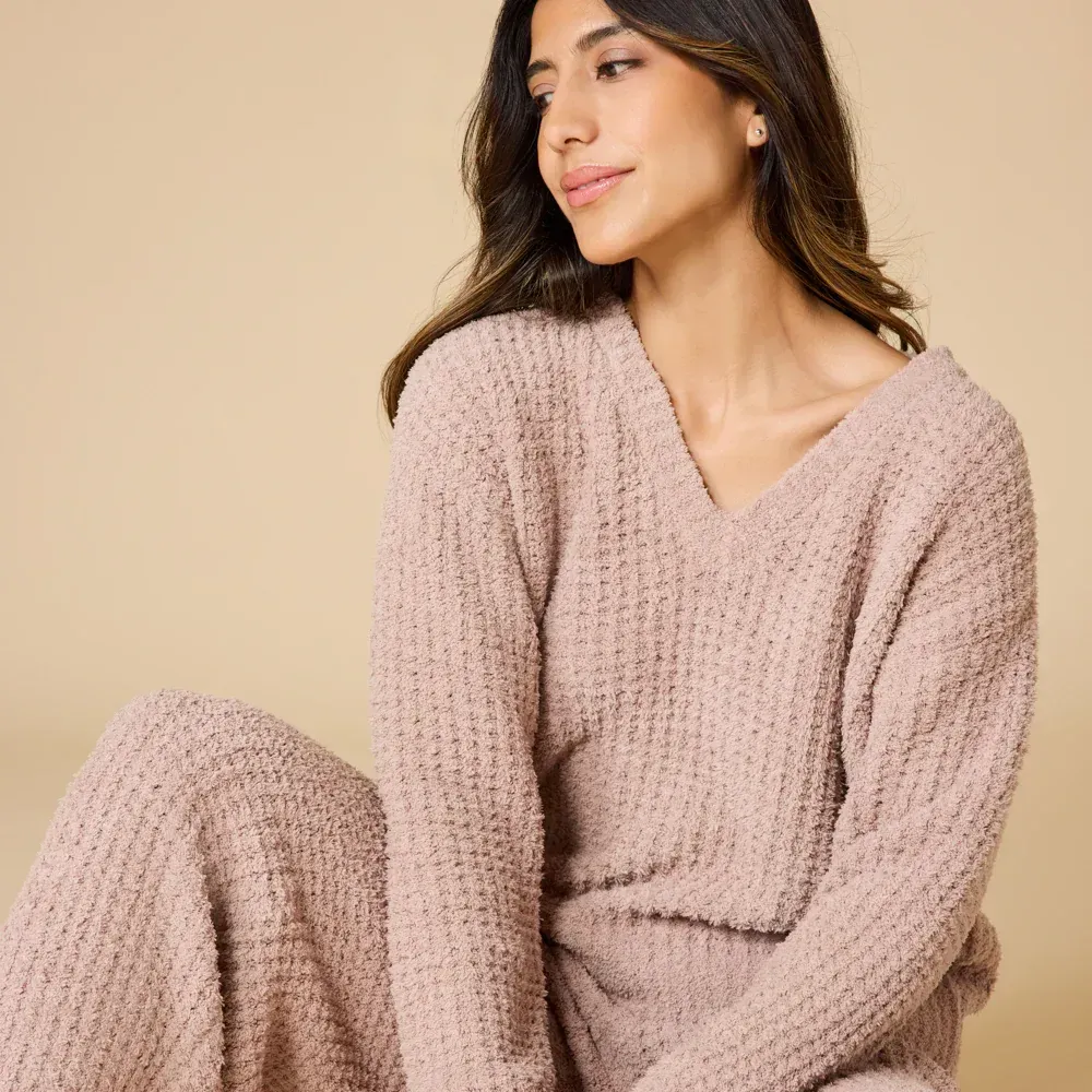 Woman in a pink, textured knit sweater and matching pants, sitting in front of a neutral background.