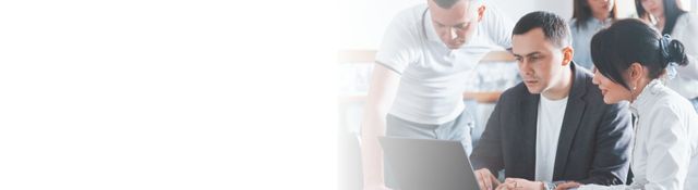 A group of people are sitting around a table looking at a laptop.