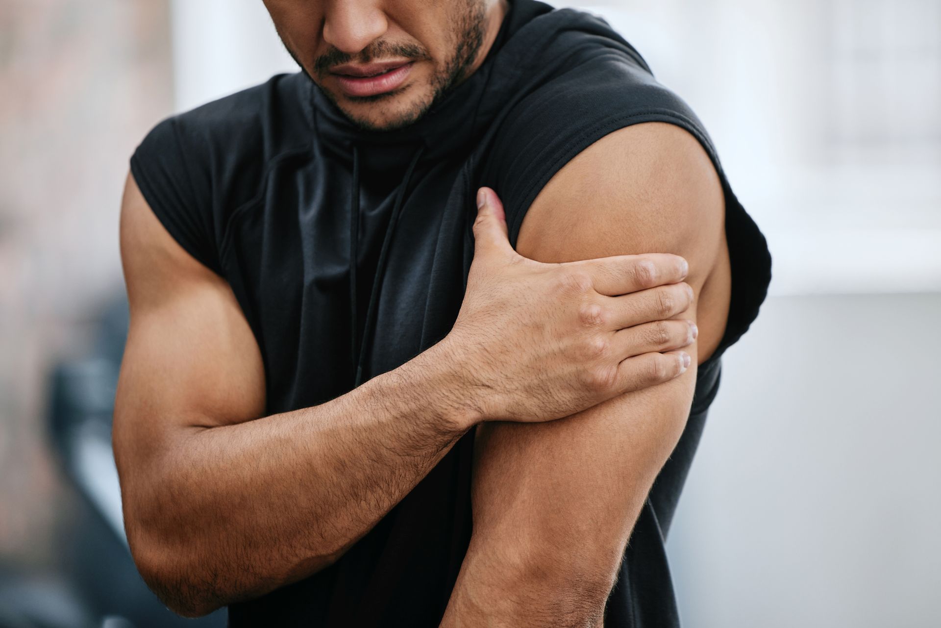 Man in black shirt clutching his left bicep in pain, at a gym.