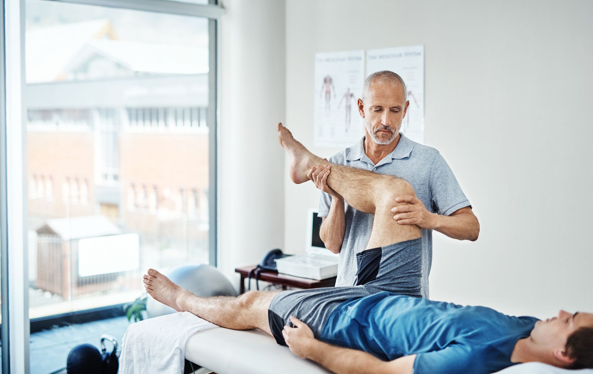 Physiotherapist examining a patient's leg in a bright room.