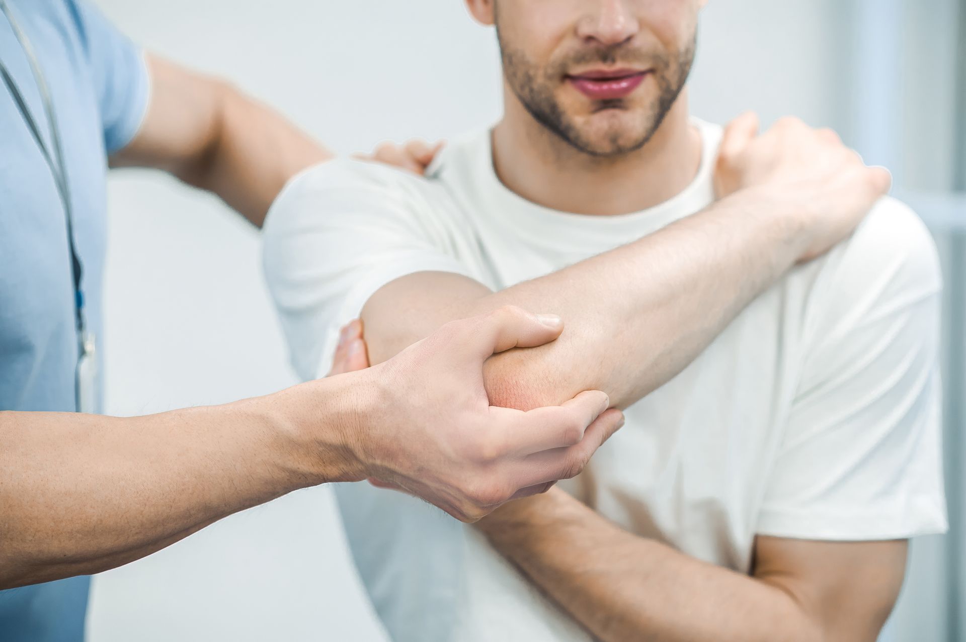 Man receiving physical therapy on his elbow; therapist in blue shirt.
