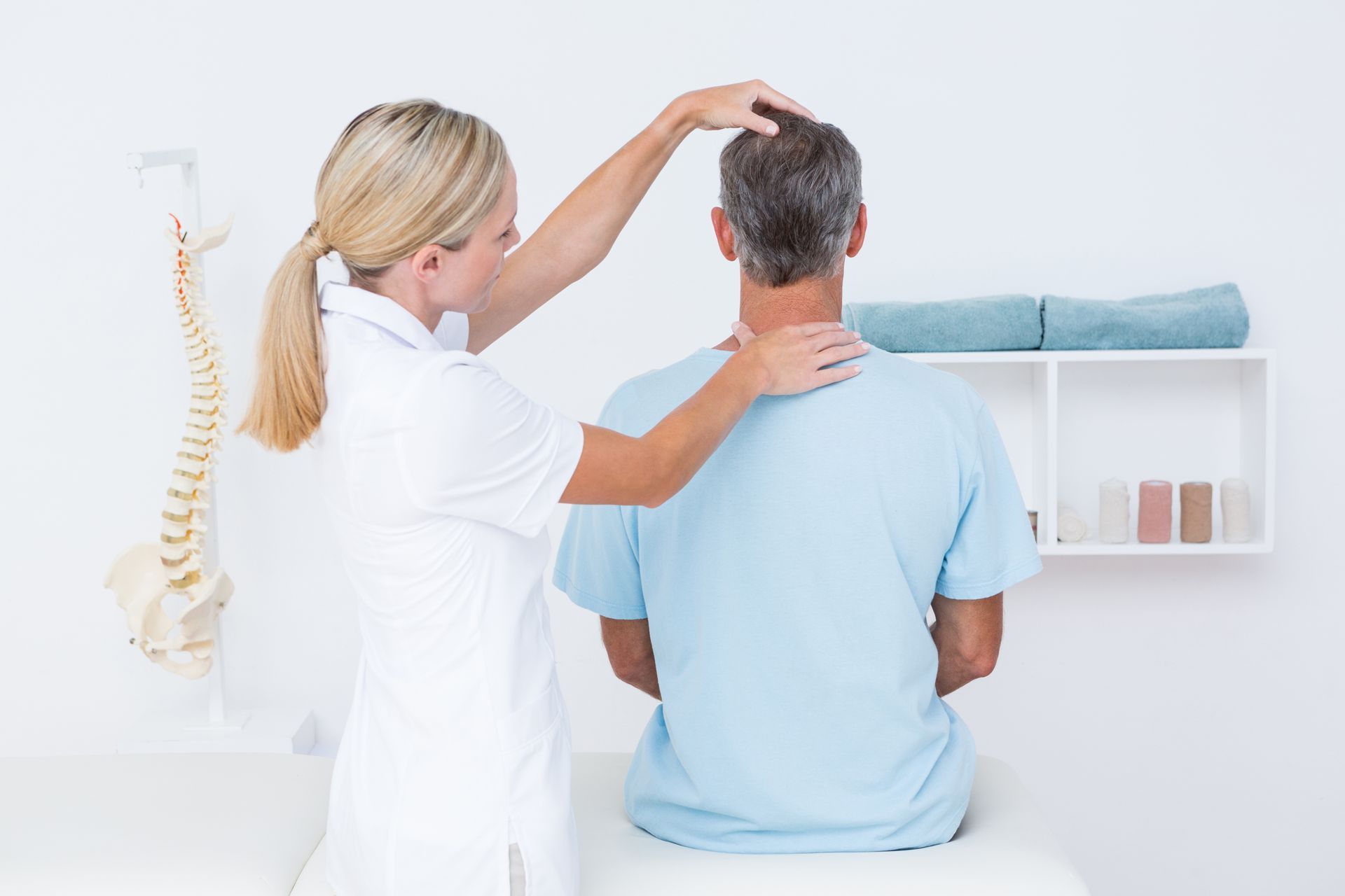 A woman is examining a man 's neck while he sits on a table.