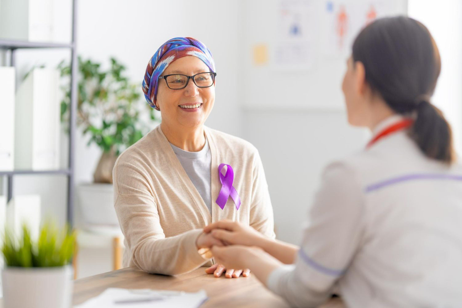 A woman with cancer is holding the hand of a nurse.