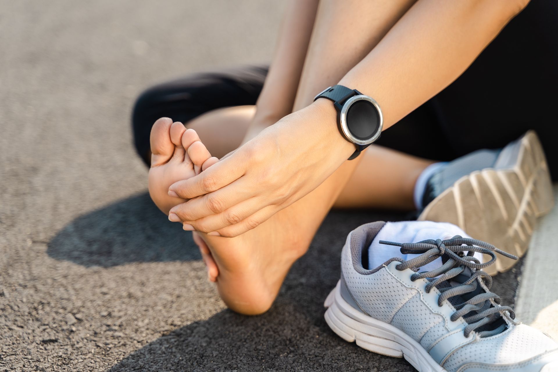 A woman is sitting on the ground holding her foot while wearing a smart watch.