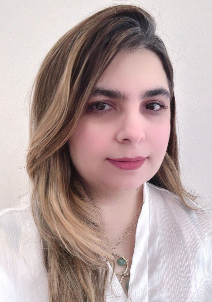 A woman with long hair is wearing a white shirt and a necklace.