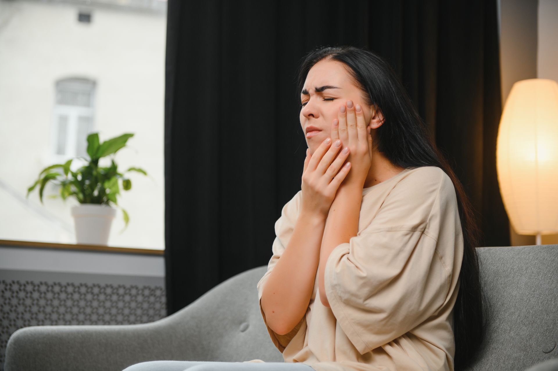 A woman is sitting on a couch with a toothache.