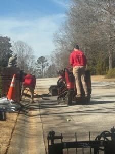 A concrete irrigation canal runs through green rice fields, with houses in the background under a cloudy sky.