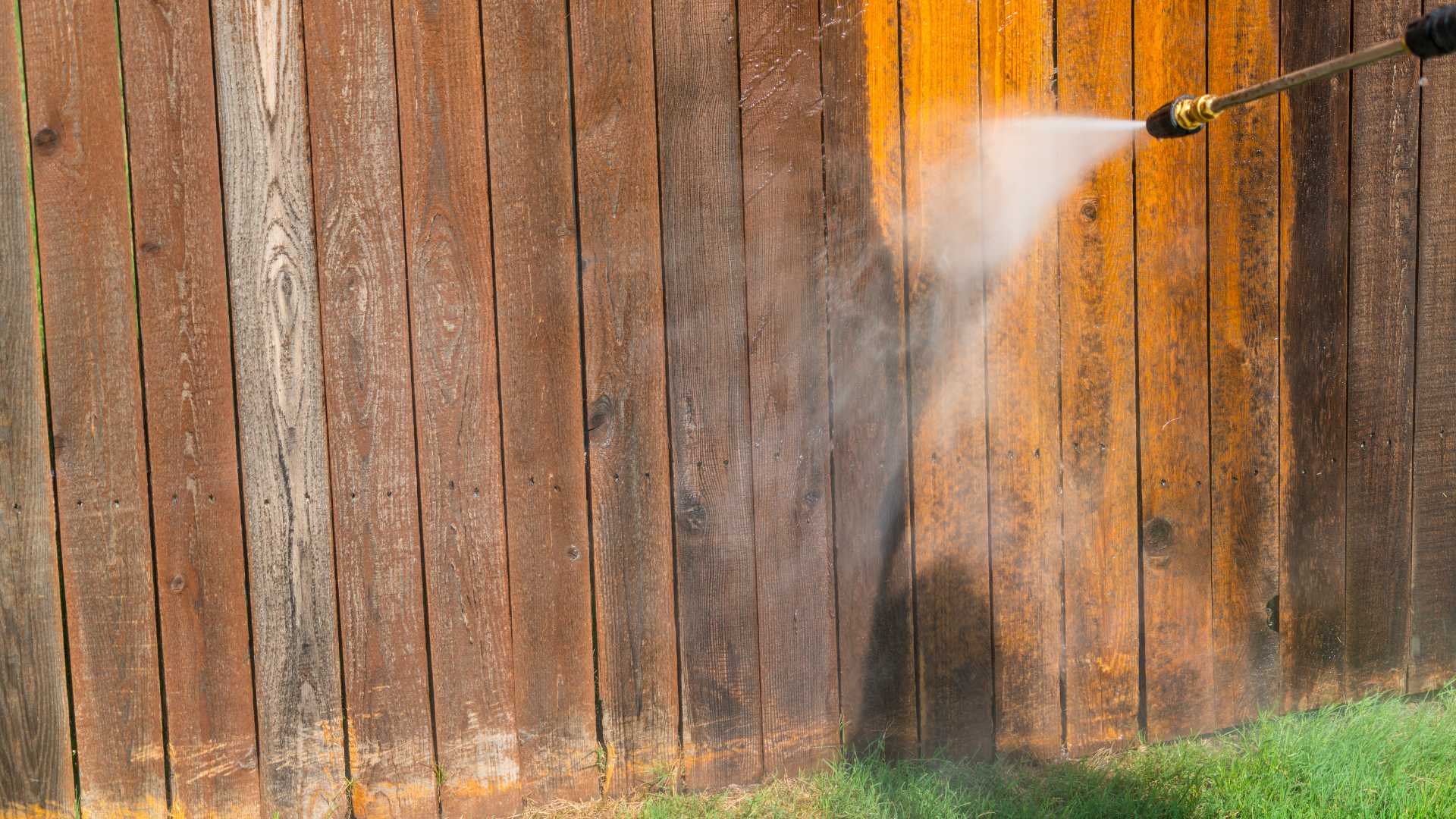 Power washer cleaning a weathered wooden fence.