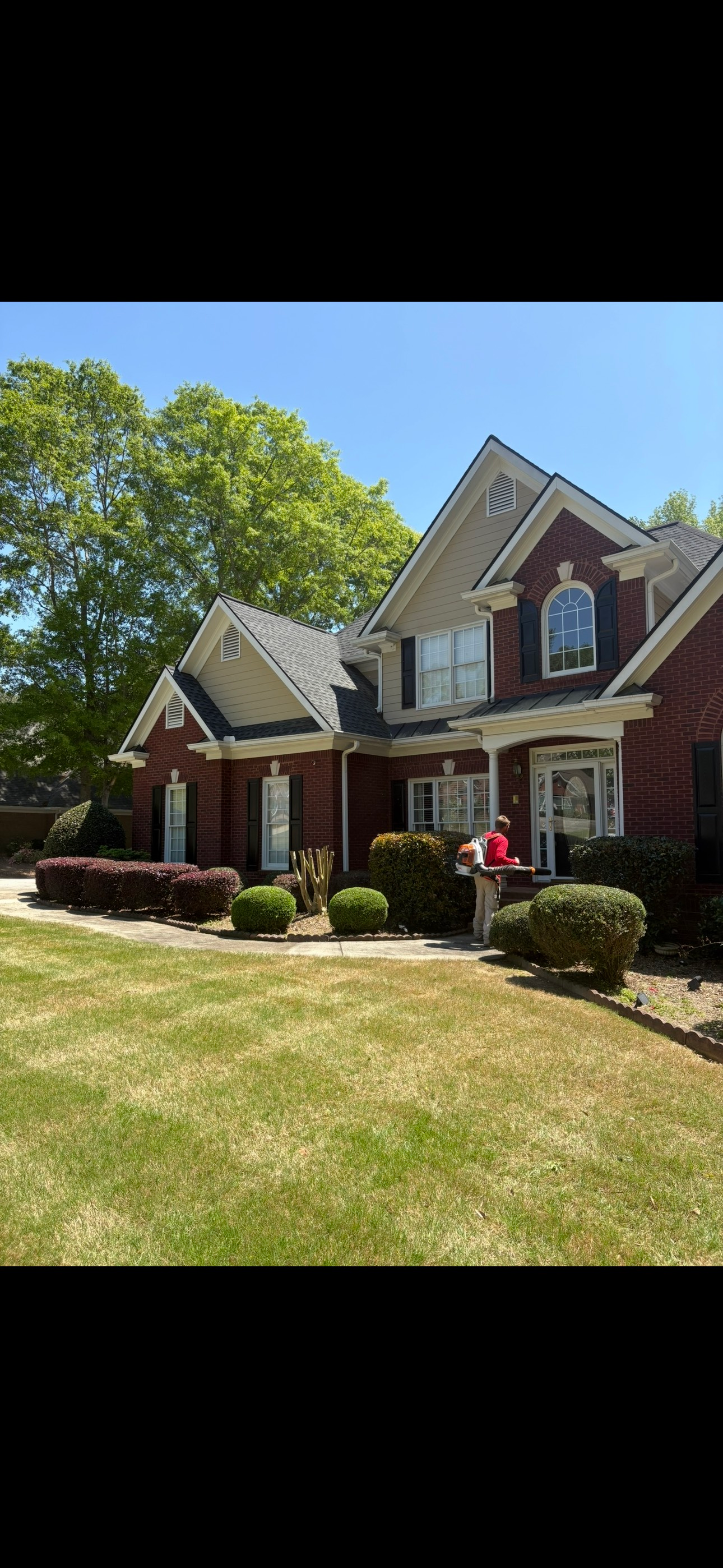 A brick house with landscaping, bushes and greenery along the front, and a curved lawn.