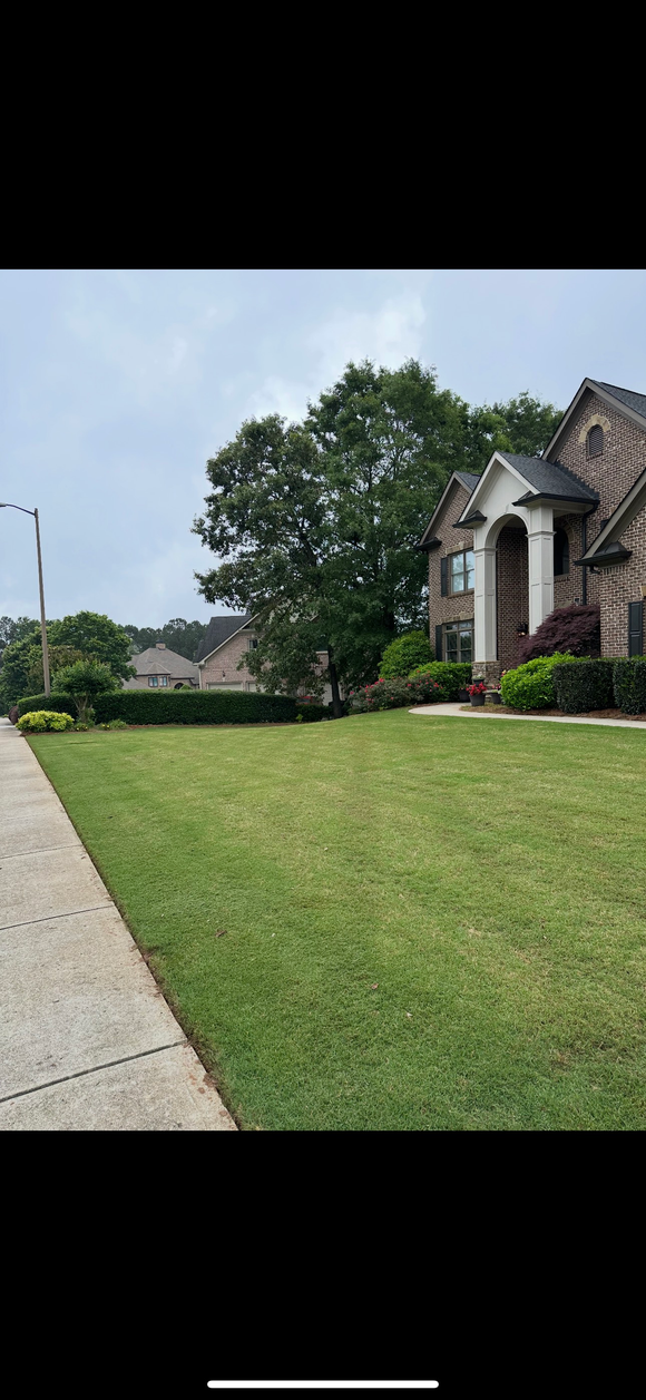 Man in cap and gloves working on irrigation system in a grassy yard.