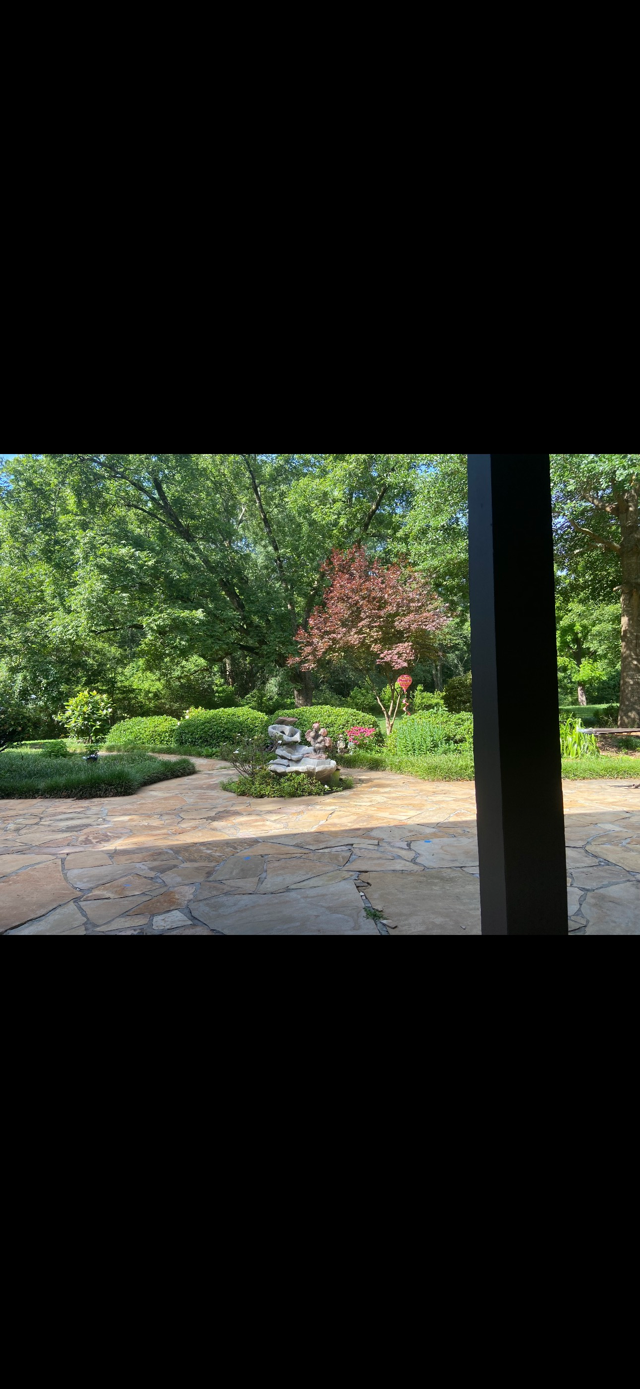 View from a porch of a garden with lush greenery, including a bench and a reddish tree.