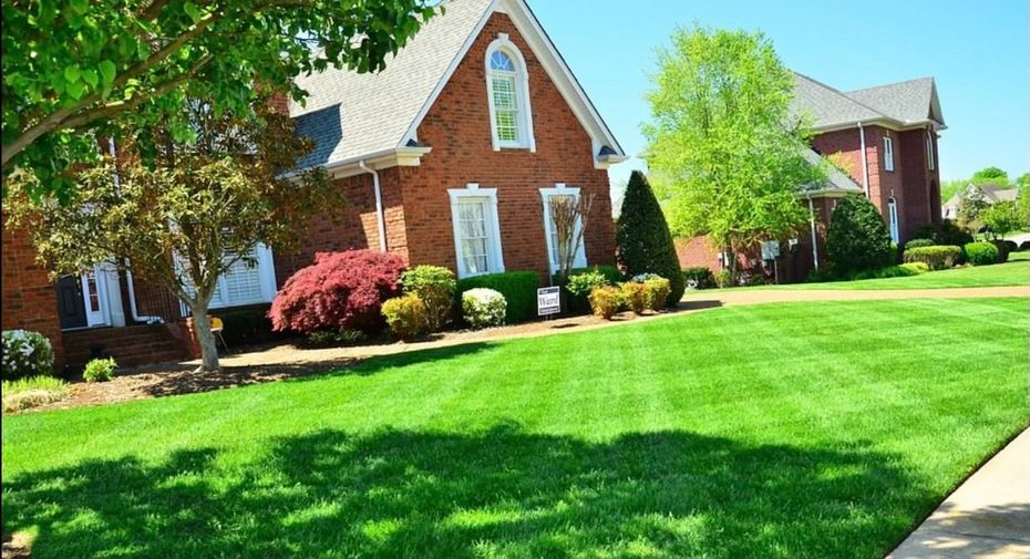 Brick house with lush green lawn and trees on a sunny day.