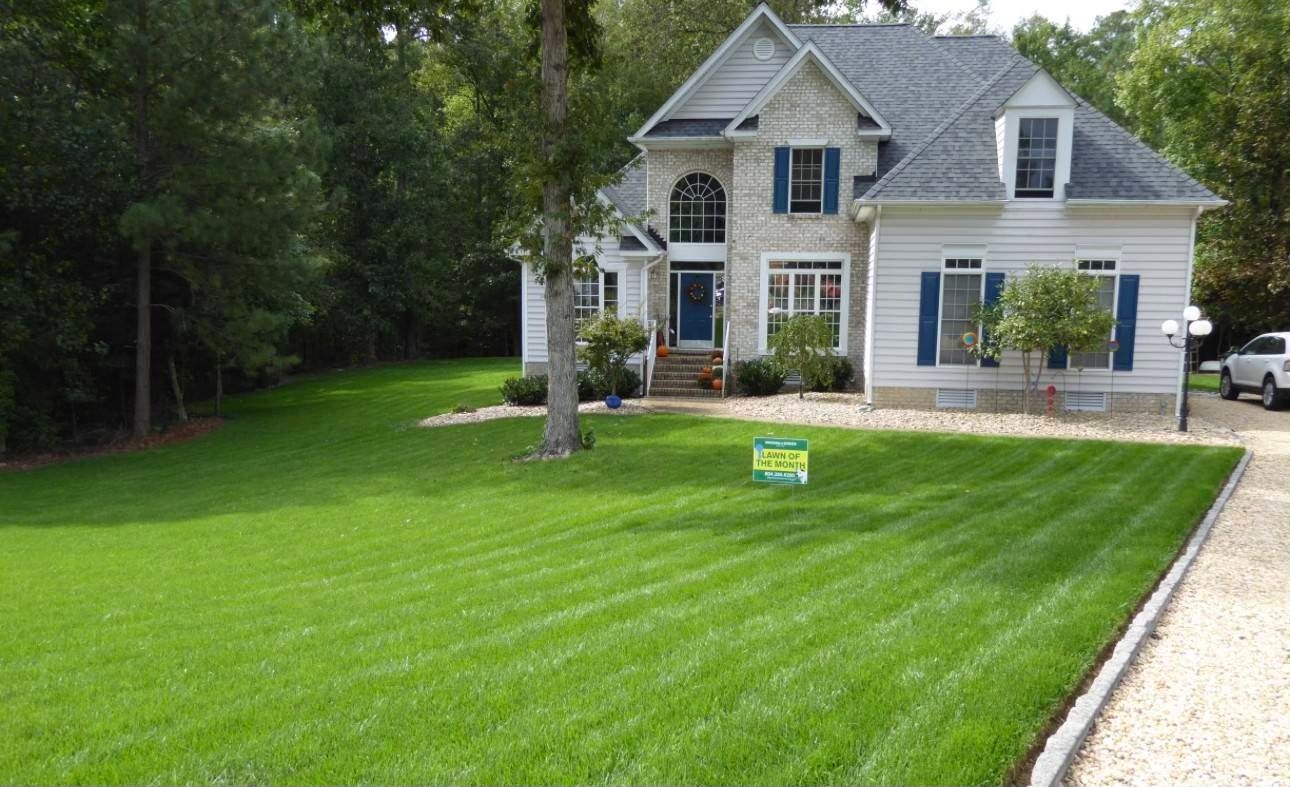 Well-manicured lawn in front of a two-story house with stone facade and blue accents.