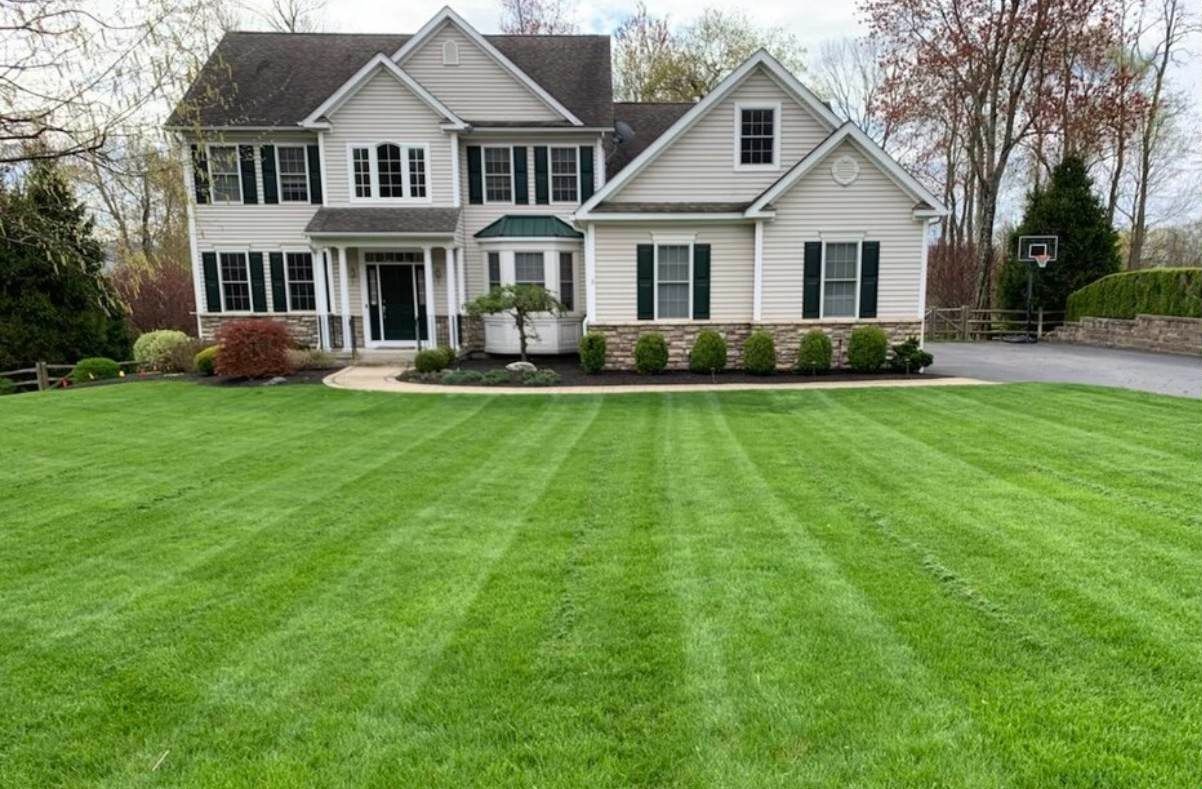 Two-story house with a well-manicured lawn; green stripes created by mowing, green and tan colors.