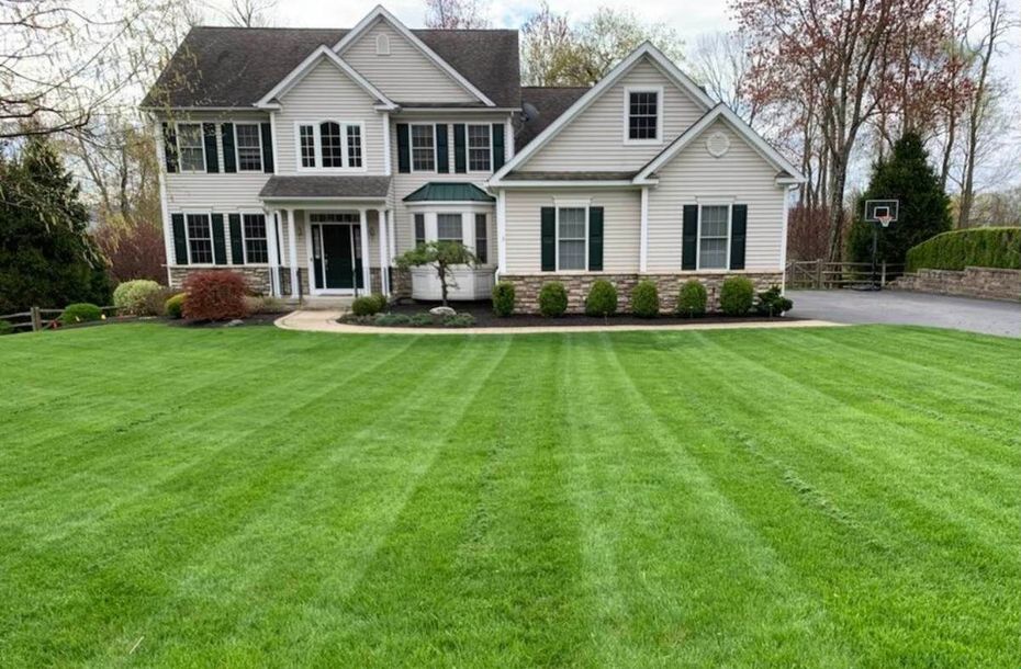 Two-story house with a well-manicured lawn; green stripes created by mowing, green and tan colors.