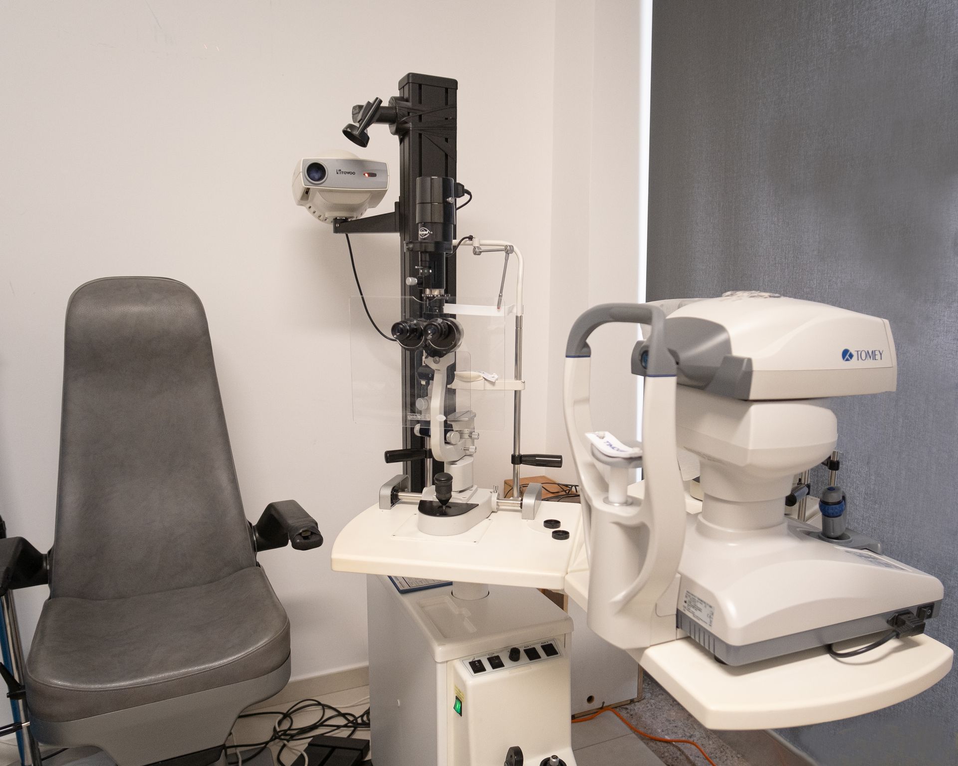 Una postazione optometrica con poltrona reclinabile per il paziente, lampada a fessura e autorefrattometro da tavolo su un tavolo bianco.