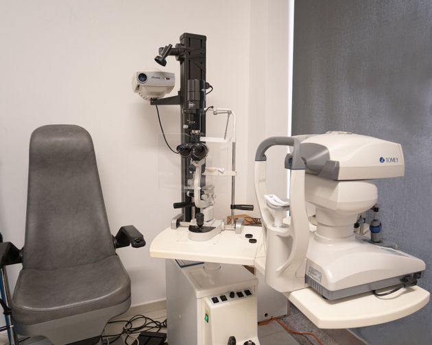 Una postazione optometrica con poltrona reclinabile per il paziente, lampada a fessura e autorefrattometro da tavolo su un tavolo bianco.