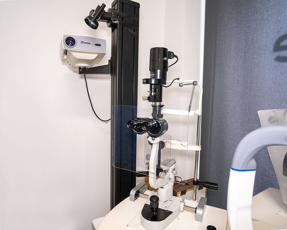 Un microscopio oftalmico a lampada a fessura per esami oculistici, posizionato su un tavolo contro una parete bianca.