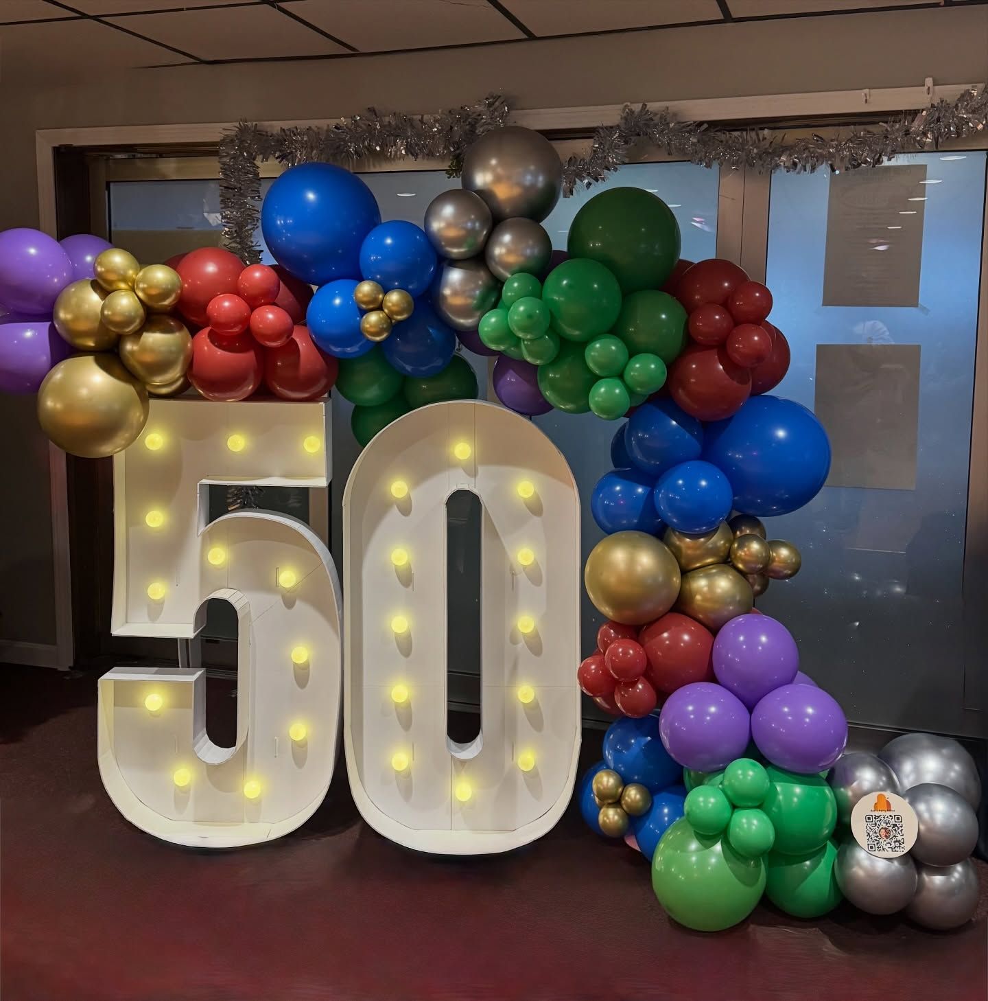 50th birthday balloon display with lit marquee numbers and colorful balloons on a doorway backdrop