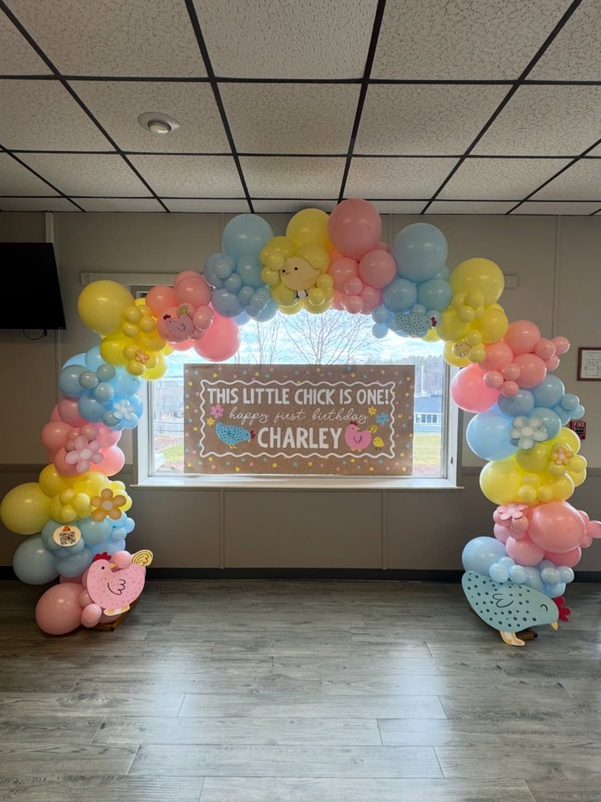 Pastel balloon arch framing a birthday sign for Charley in a room with a projector screen
