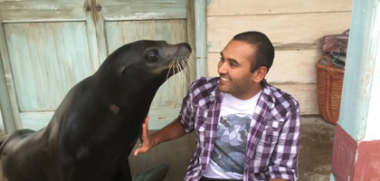 A man in a plaid shirt is sitting next to a seal.