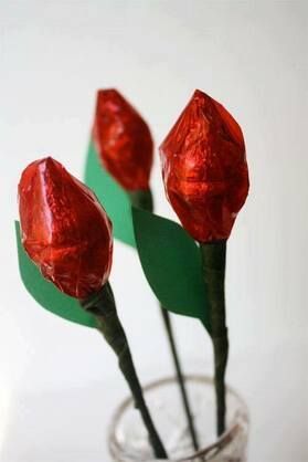 Three red roses wrapped in red foil are in a glass vase.