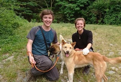 A man and a woman are kneeling next to two dogs in a field.