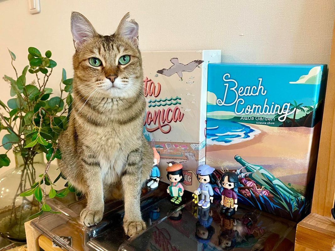 A cat is sitting on a table next to a painting of a beach.