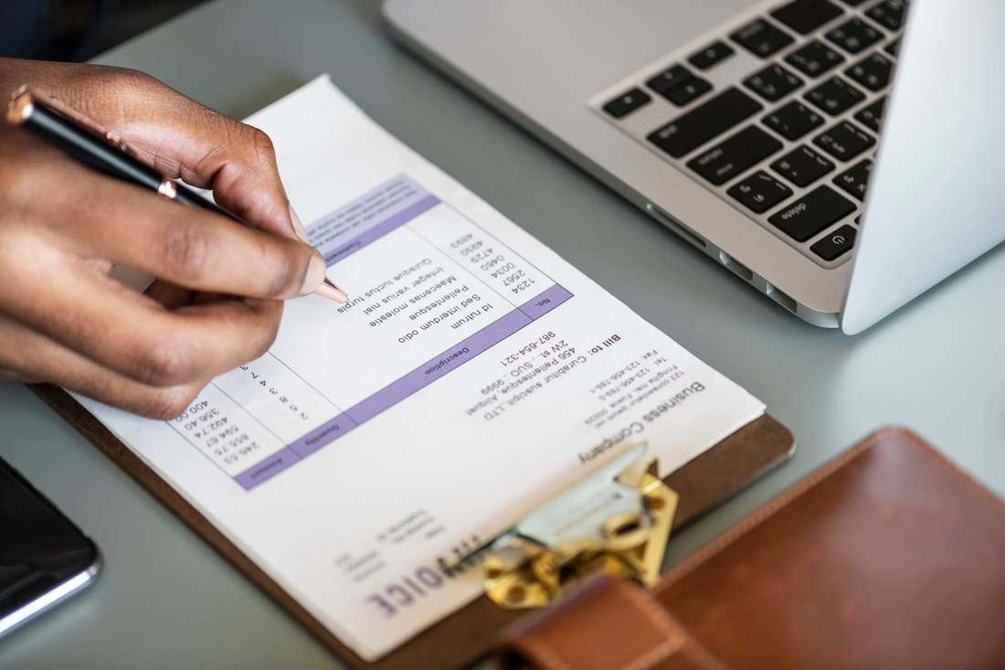 A person is writing an invoice on a clipboard next to a laptop.