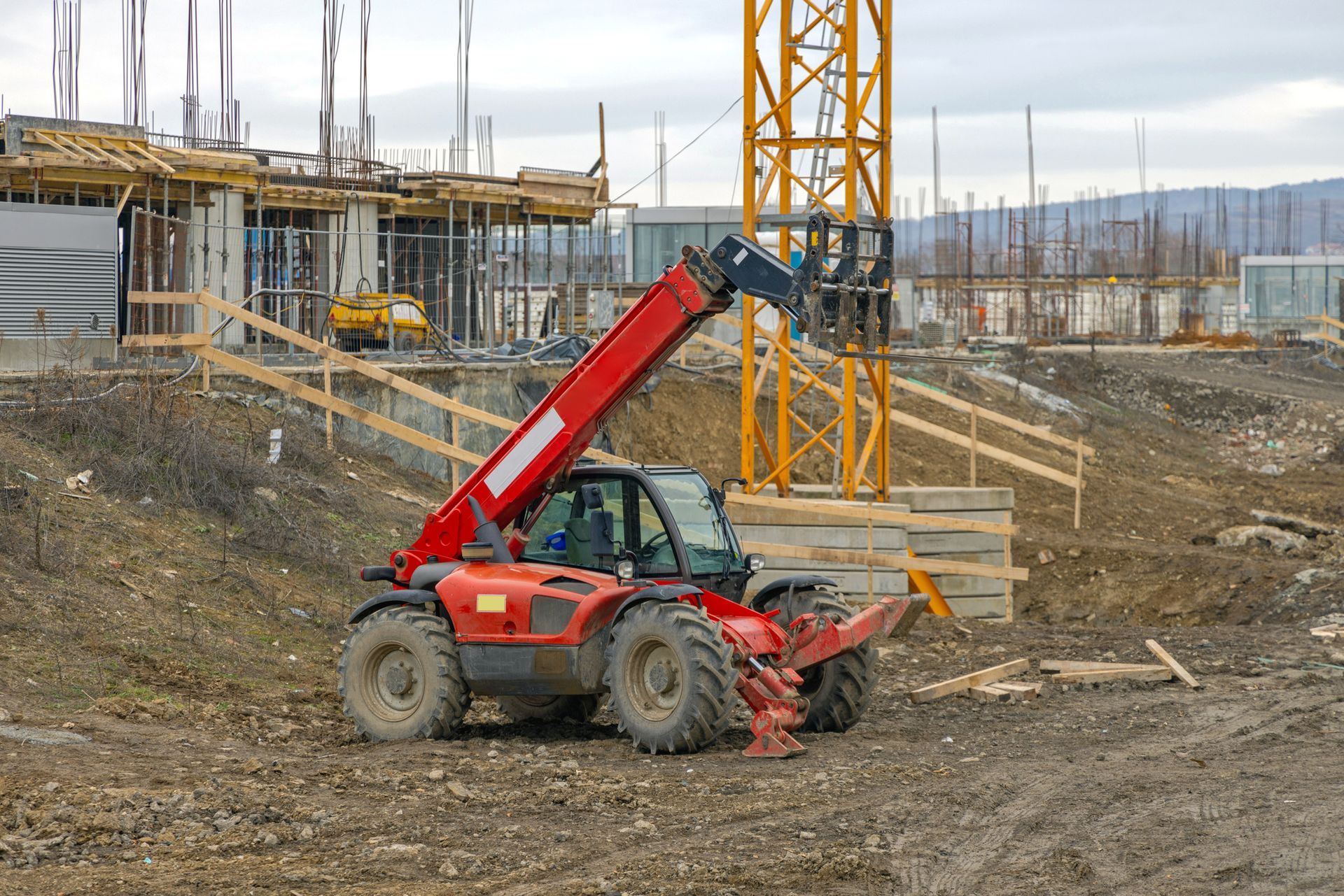A red forklift is driving down a dirt road at a construction site.